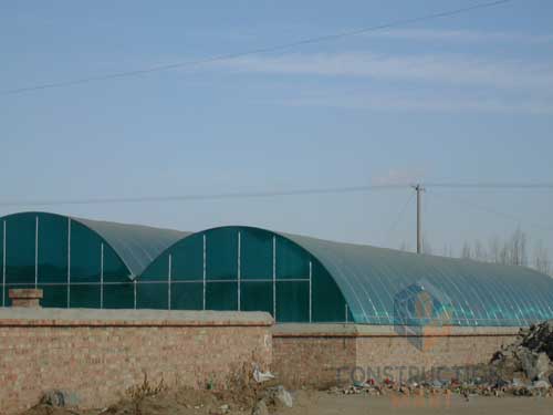 Industrial factory roof with blue X-type polycarbonate sheets forming a curved structure for weather protection and daylighting