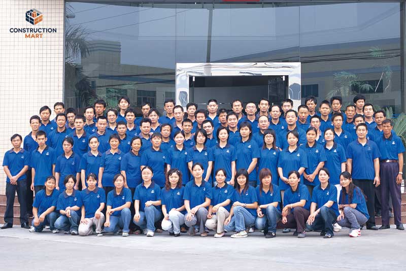 The Constructionmart team posing together in front of the company office, all wearing blue factory uniforms to represent unity and professionalism